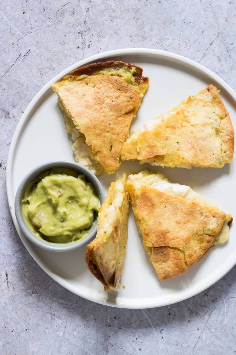four slices of air fryer chicken quesadilla served on a white plate with a small dish of guacamole