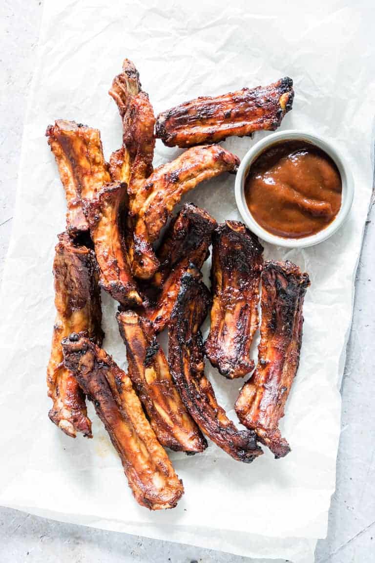 air fryer ribs on white parchment paper next to a small dish of bbq sauce