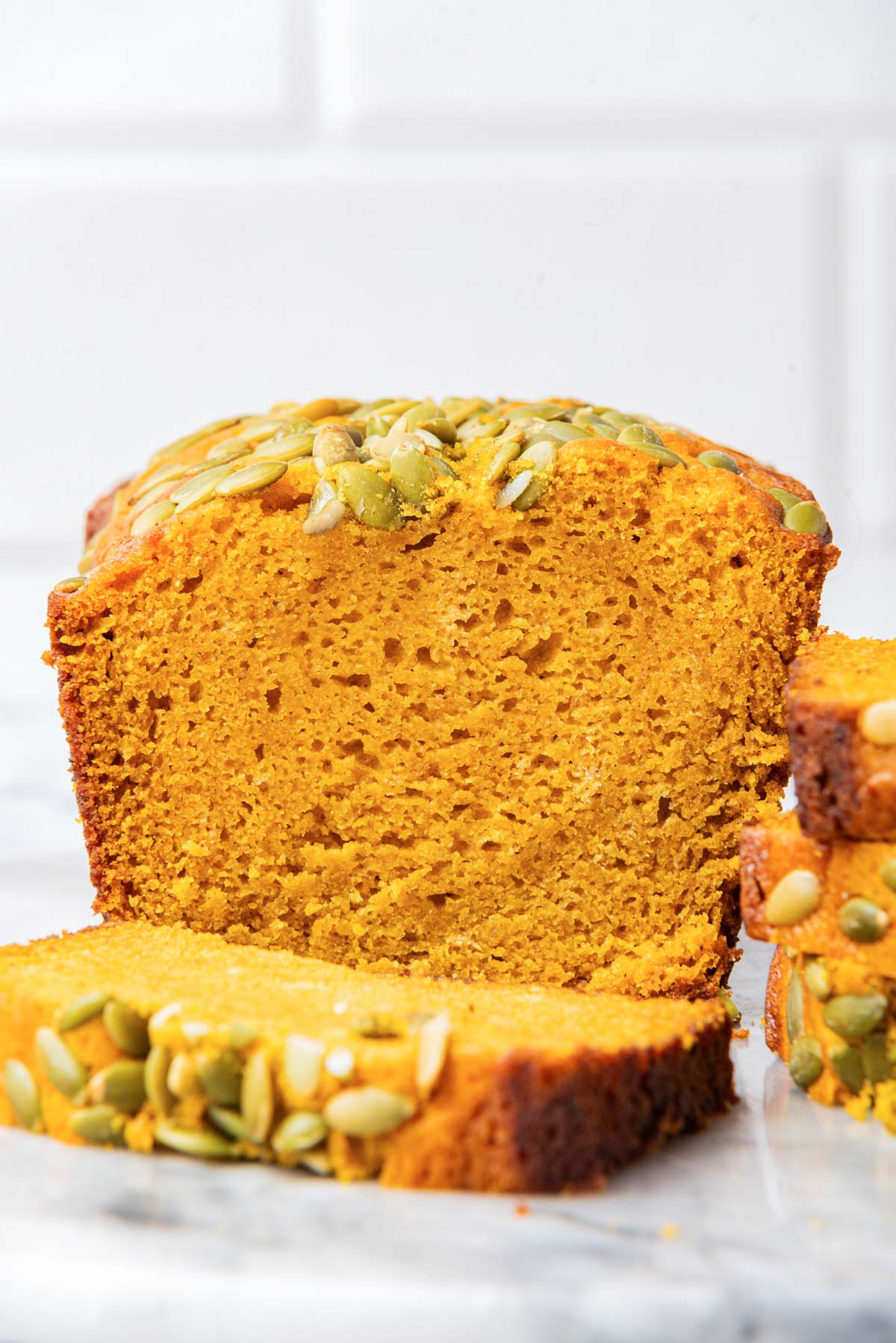 A close-up view of a sliced loaf of bread topped with pumpkin seeds, showing a dense and moist texture.