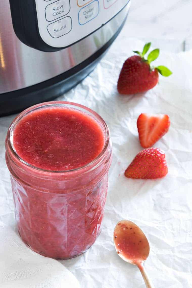 Instant Pot Strawberry Jam in a glass jar next to the Instant Pot and fresh strawberries
