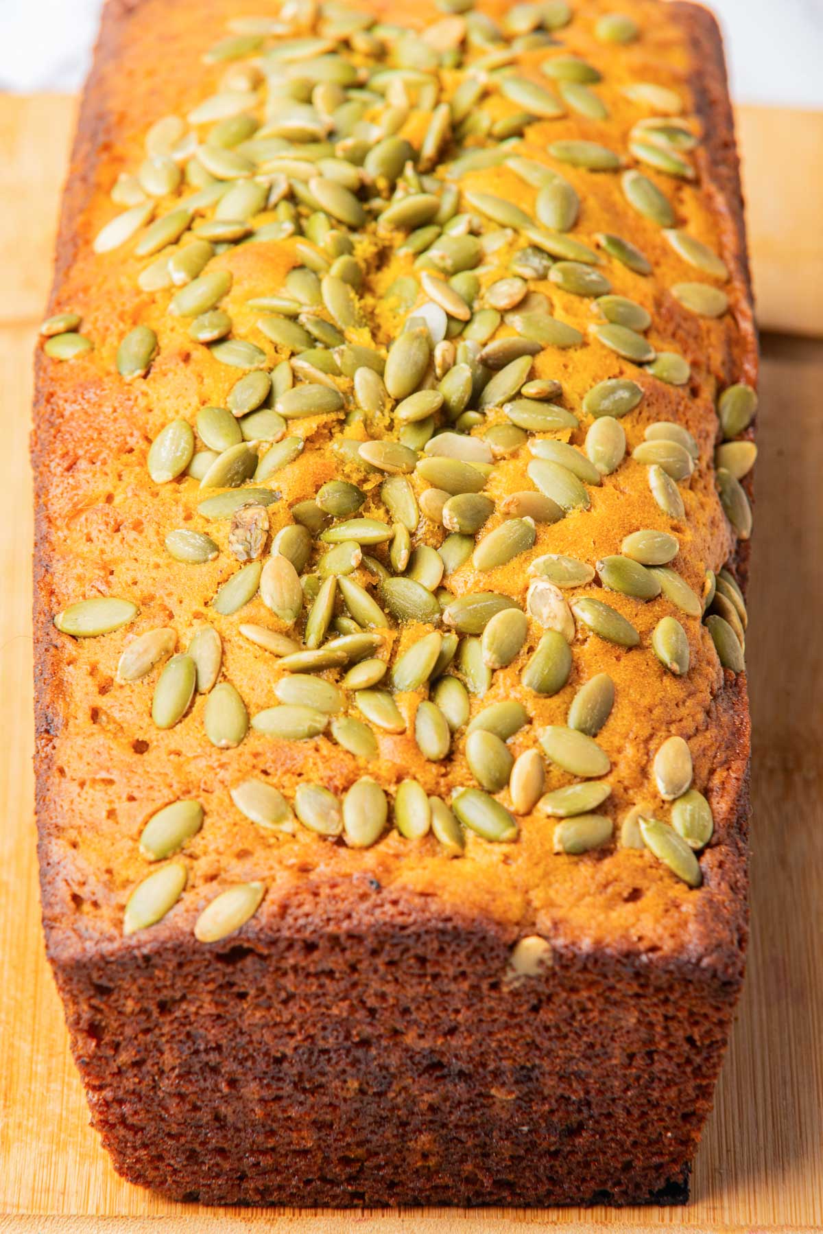 A top-down view of a loaf of pumpkin bread, showcasing the pumpkin seeds topping and golden-brown crust.