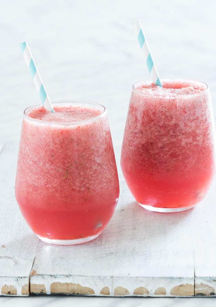 two glasses filled with strawberry watermelon smoothie and a blue striped straw