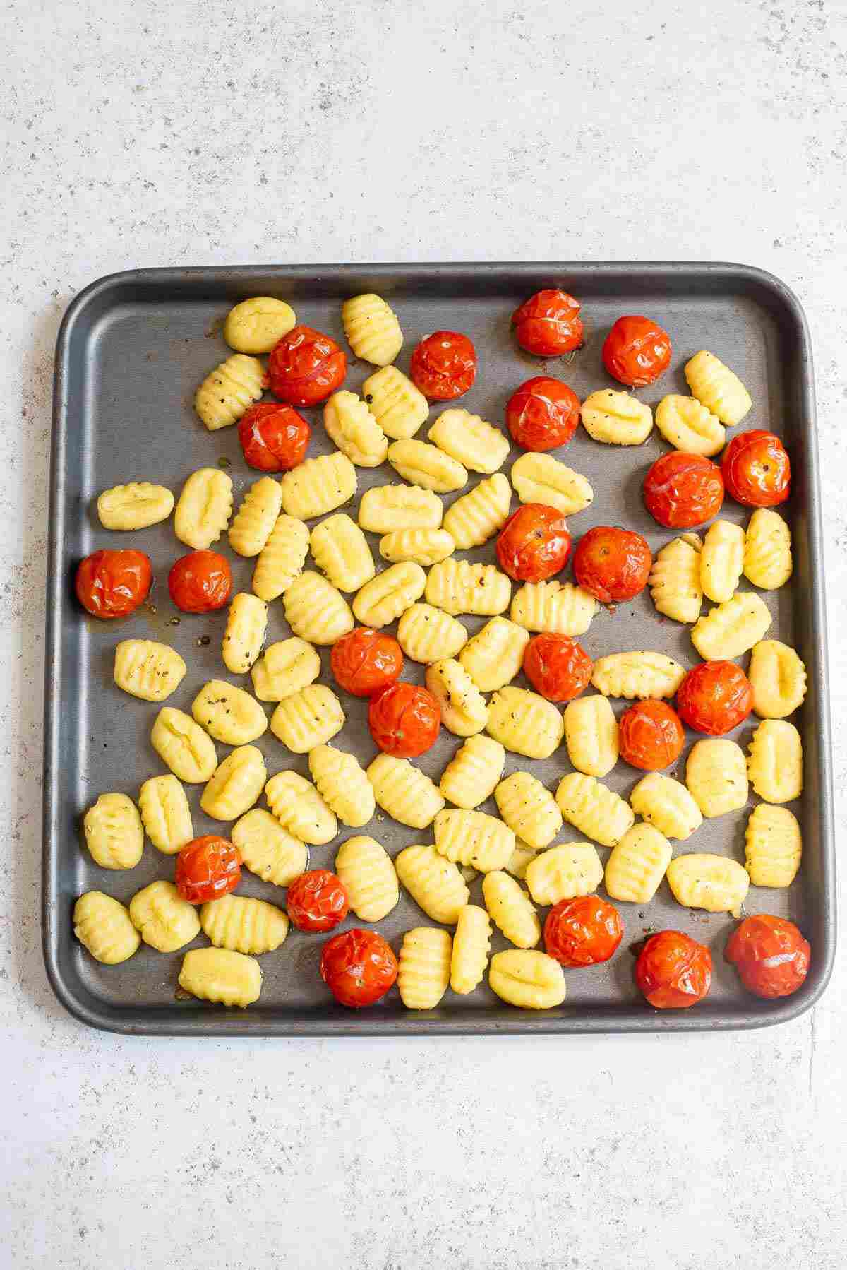 A sheet pan with gnocchi and cherry tomatoes, seasoned and ready for baking.