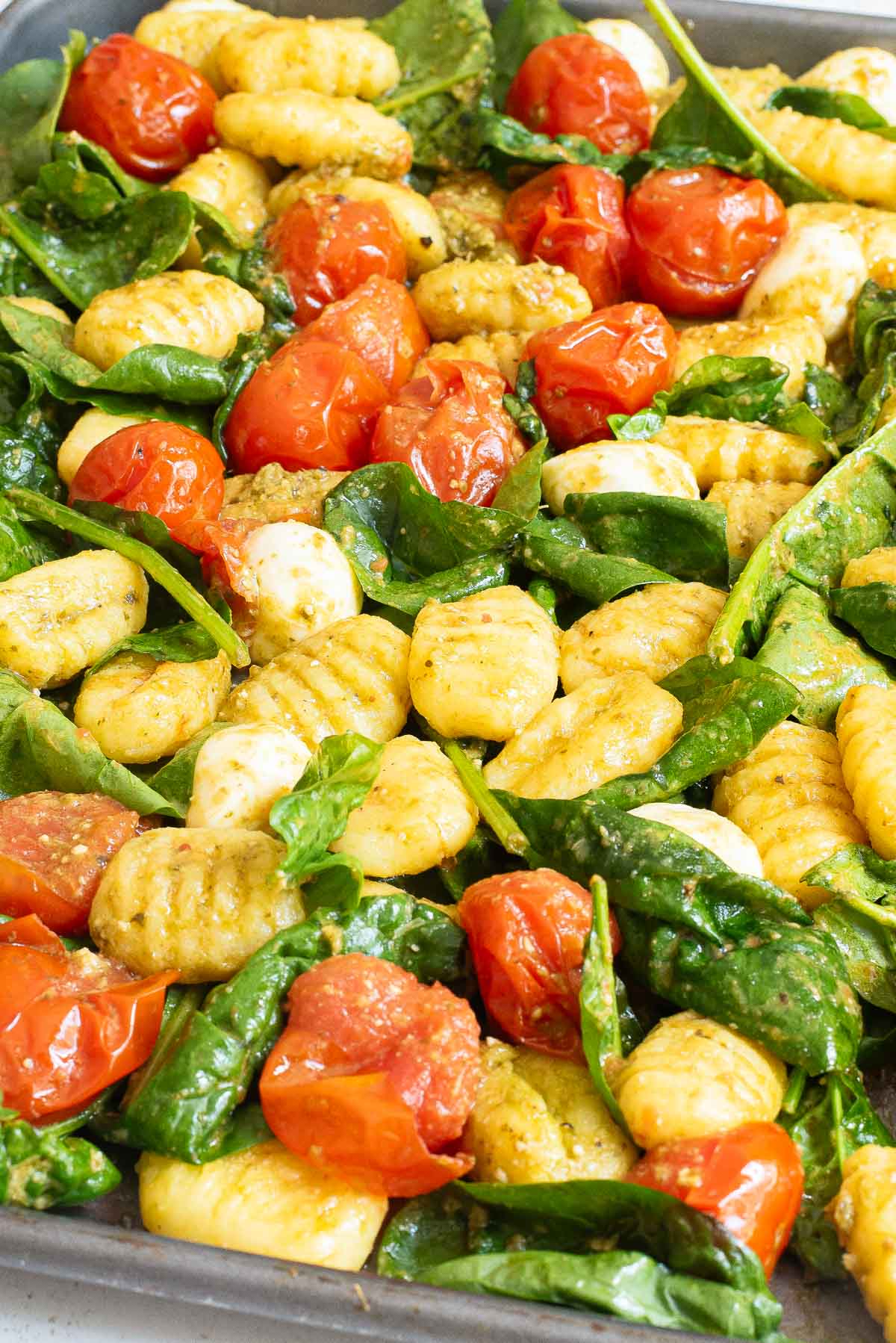 A close-up of baked gnocchi with cherry tomatoes and spinach on a sheet pan, ready to serve.