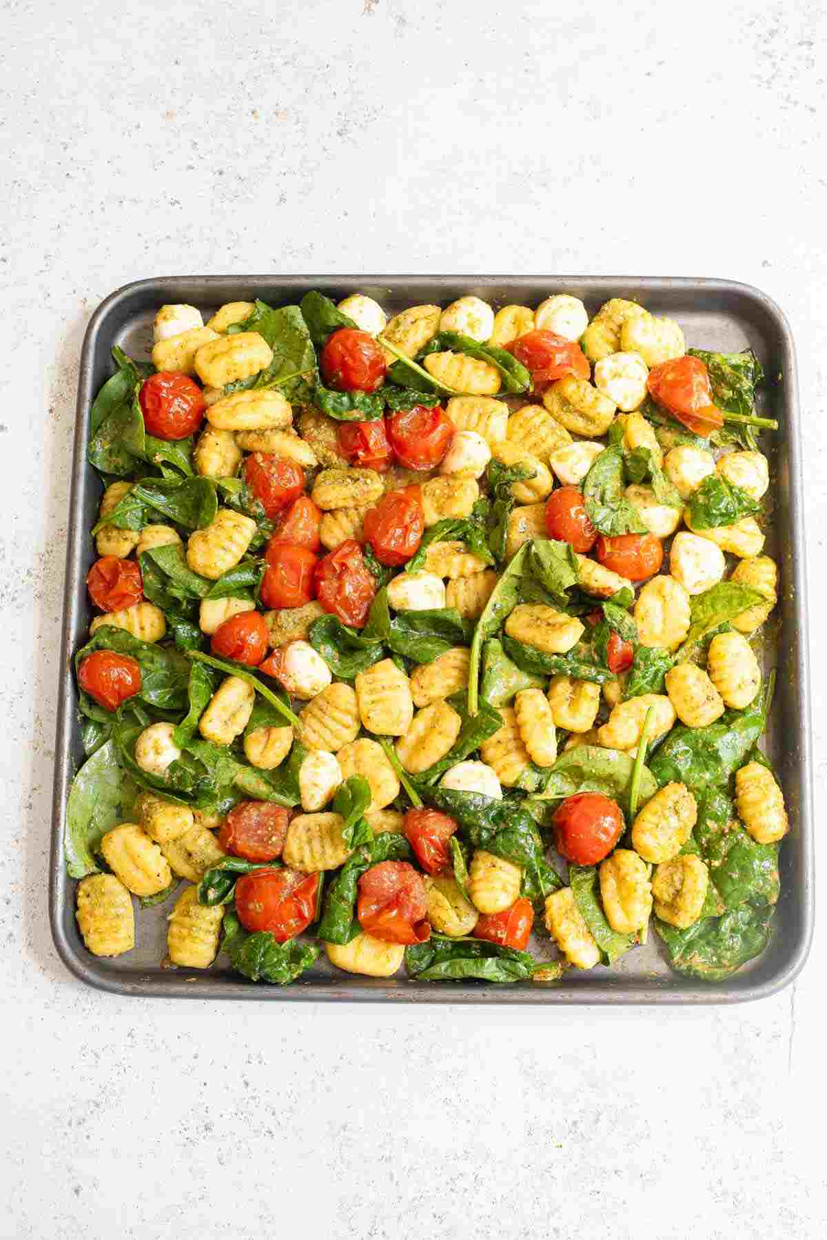 A full sheet pan with baked gnocchi, cherry tomatoes, and spinach, ready to be served.