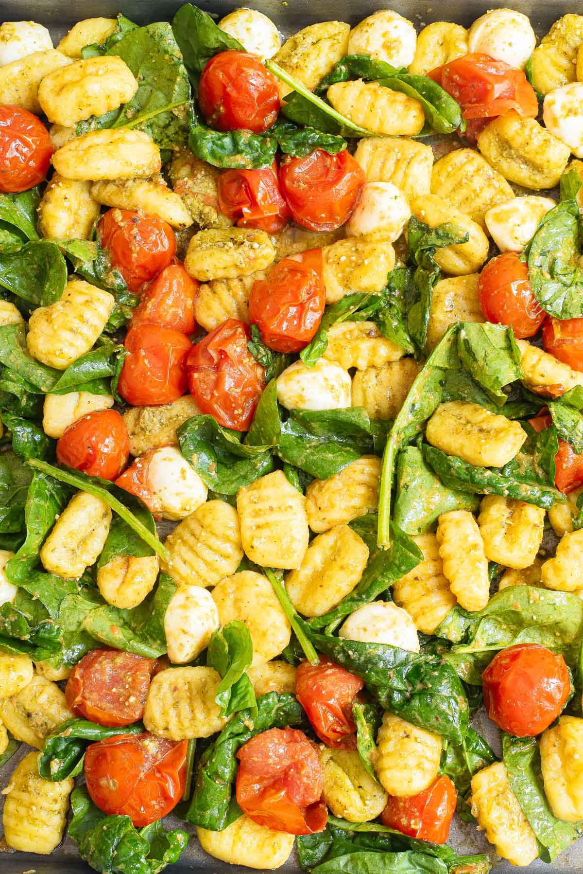 A close-up view of the sheet pan dinner, highlighting the texture of the gnocchi, tomatoes, and spinach.
