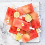watermelon margarita popsicles on a plate with flowers and lime