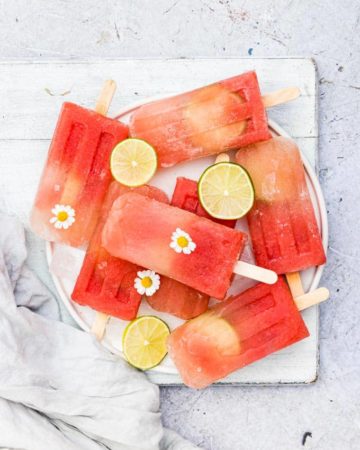 watermelon margarita popsicles on a plate with flowers and lime