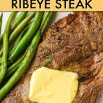 close up of ribeye steak with a pat of butter on it and a side of green beans