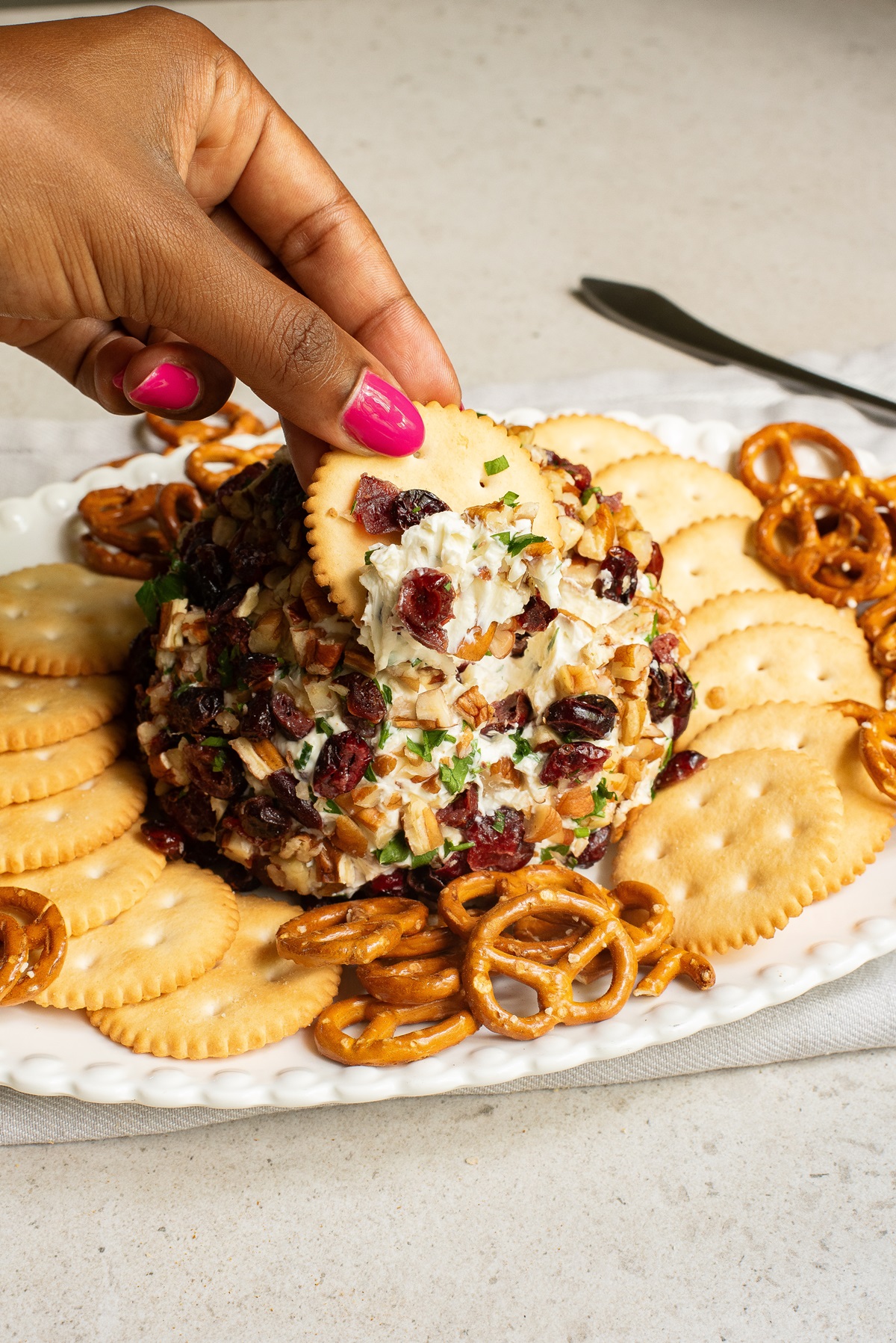 A cracker being used to take some of the cranberry pecan cheeseball.