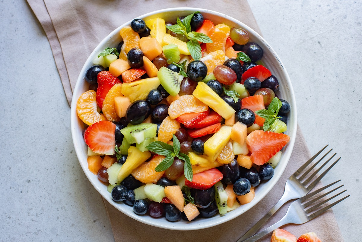Close up view of various fruits in a serving bowl with a dressing over.