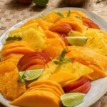 Peach, mango and orange salad on a white plate with garnish.