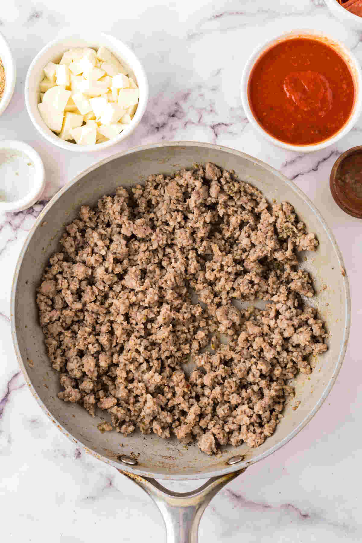 Ground sausage browning in a skillet with other ingredients prepped in bowls nearby.
