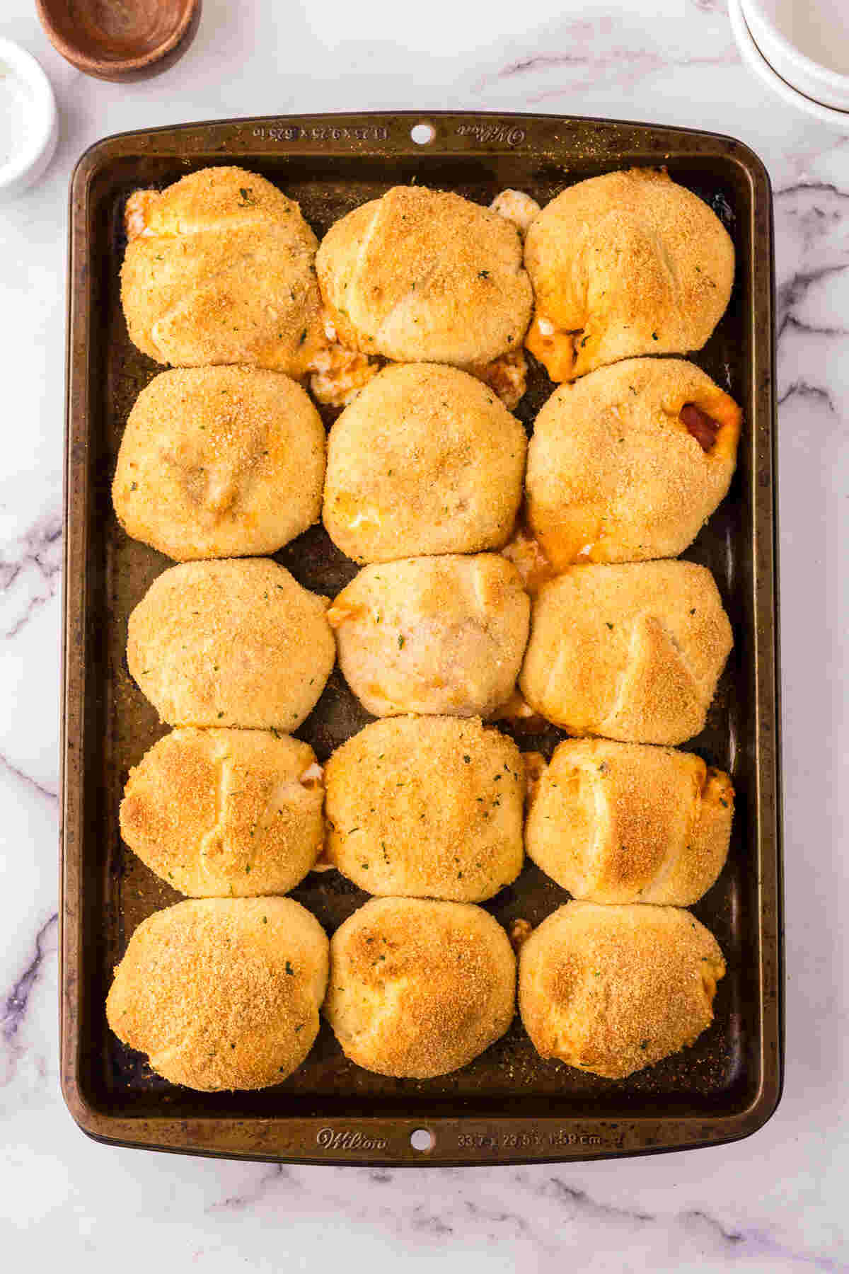 Freshly baked, golden-brown stuffed dough balls on a baking sheet, hot and ready to serve.