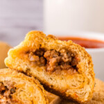 Close-up of the inside of a sliced stuffed dough pocket, with a bowl of marinara in the background.