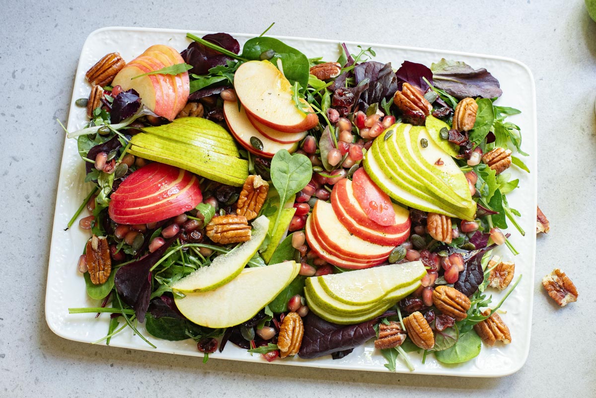 A salad with pears, apples, pecans, nuts and greens on a white plate.