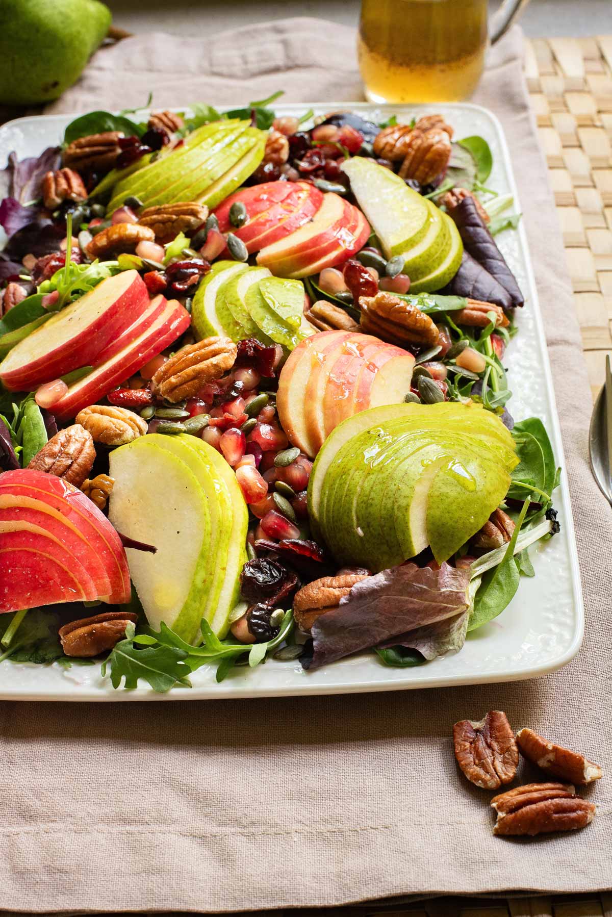A salad with pears, apples and pecans on a white serving plate.