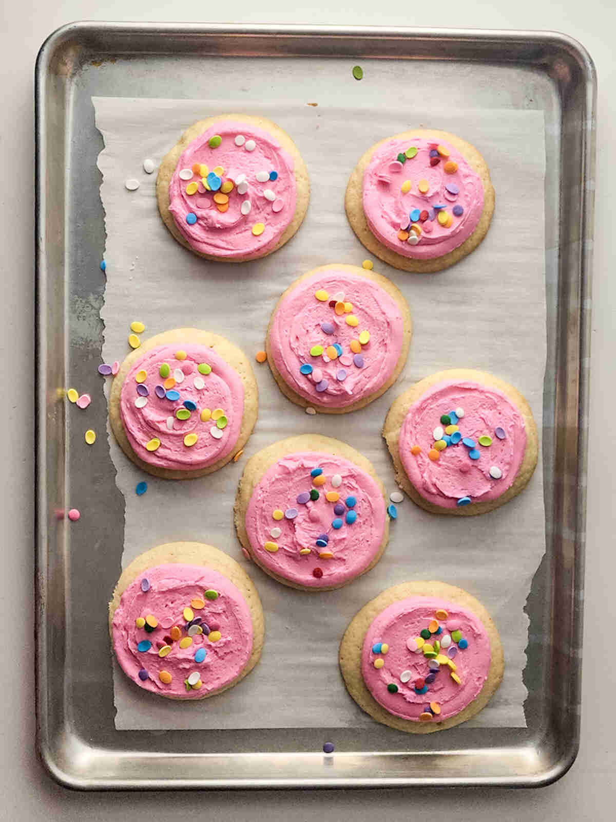 Frosted pink cookies on a baking tray with sprinkles.