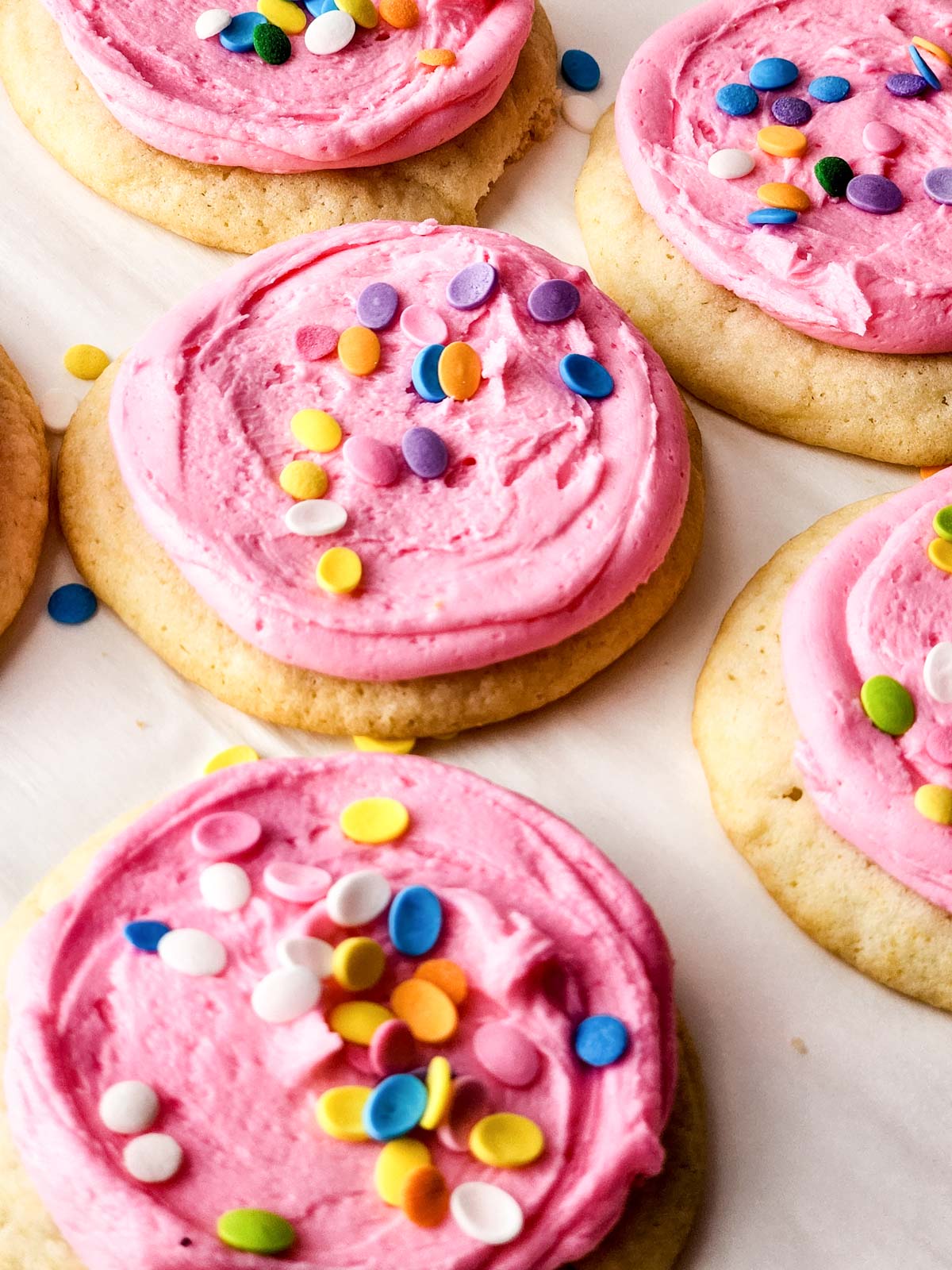 Cookies with pink frosting and sprinkles on a baking tray.