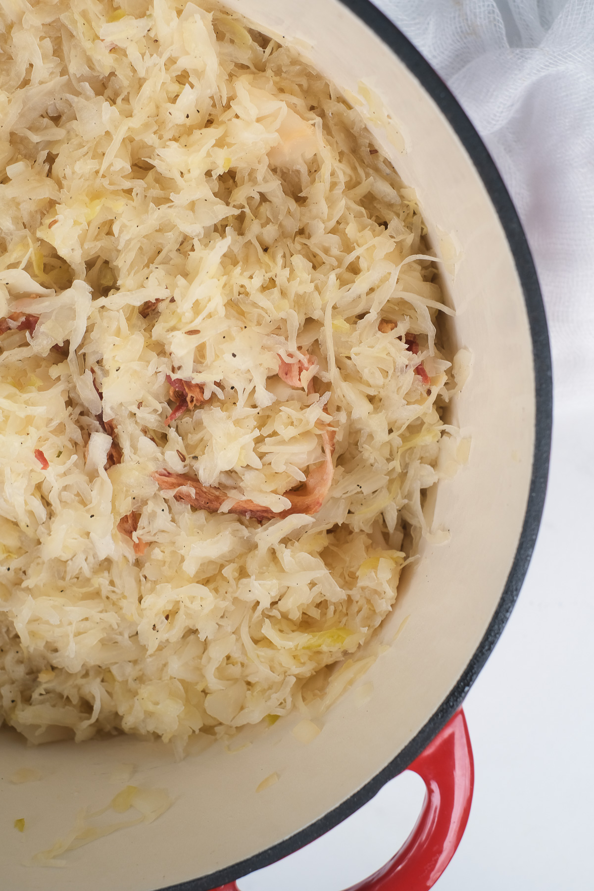 Close up view of sauerkraut with bacon bits in a red pot.
