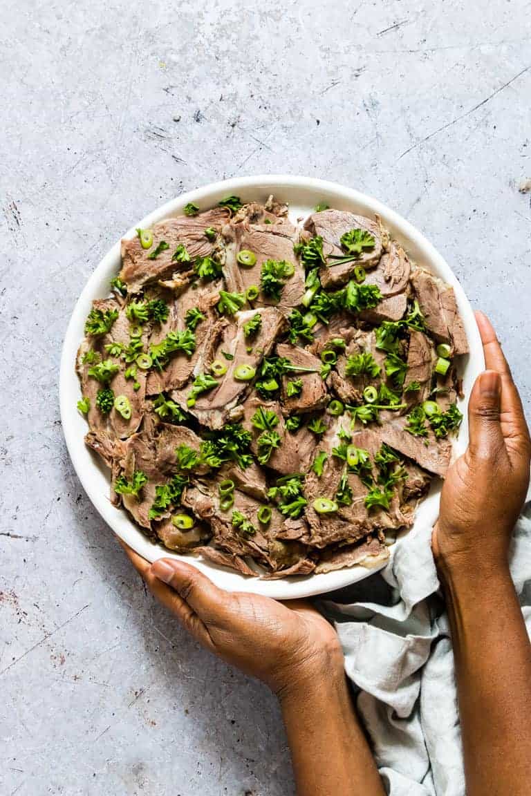 A platter of Instant Pot Lamb Shoulder sliced and garnished with parsley and green onions