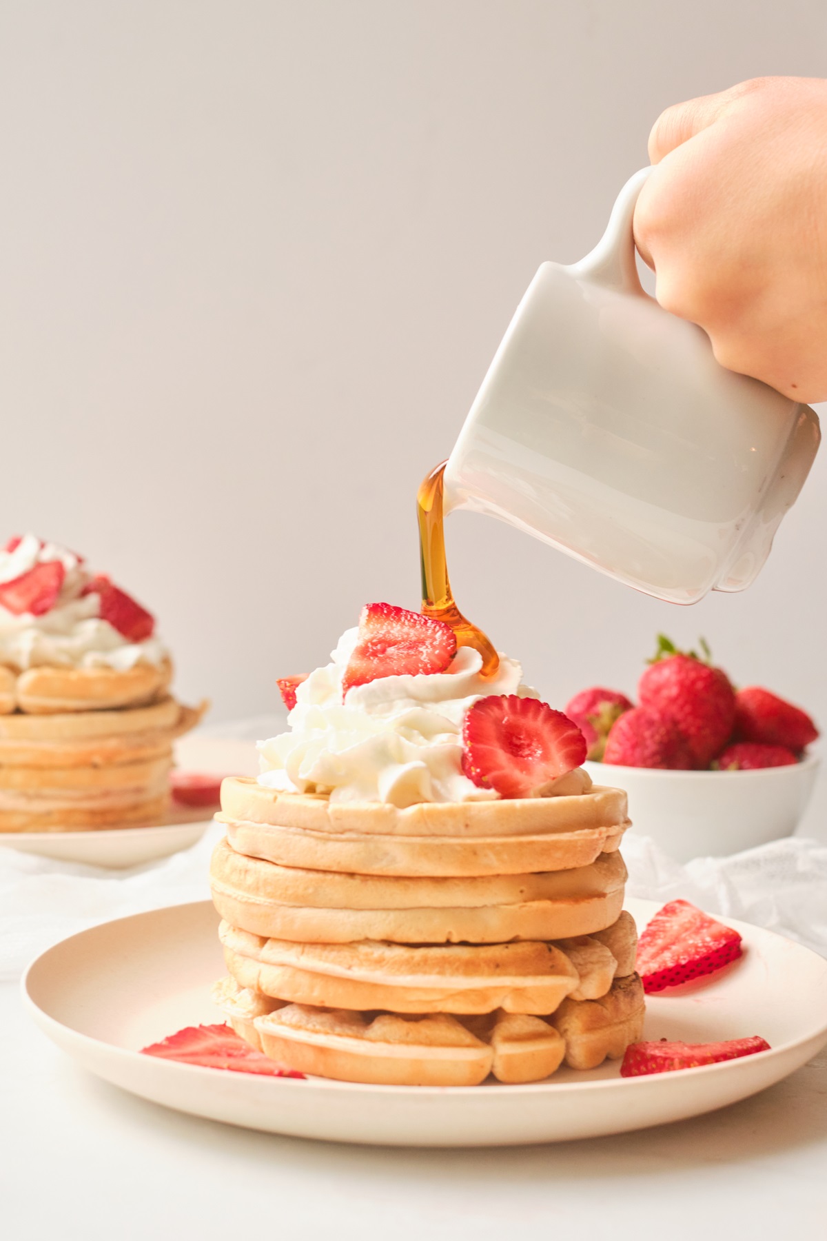 Syrup being poured onto a strawberry waffle recipe stack.