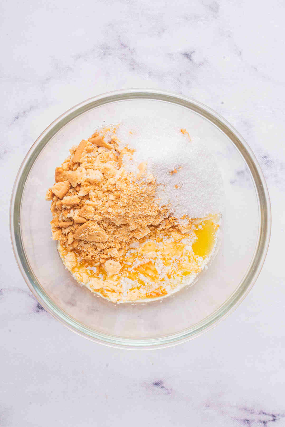 A mixing bowl containing graham cracker crumbs, sugar, and melted butter being stirred to form a base for ice cream.