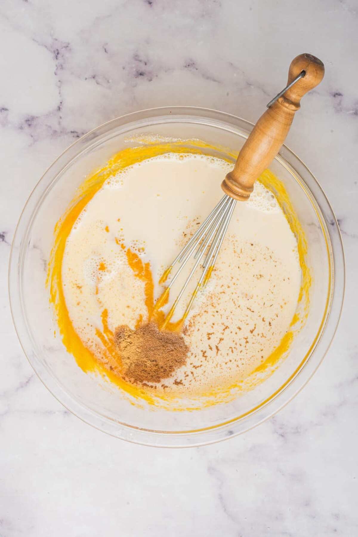 Adding spices to the pumpkin pie filling mixture in a glass bowl with a whisk.