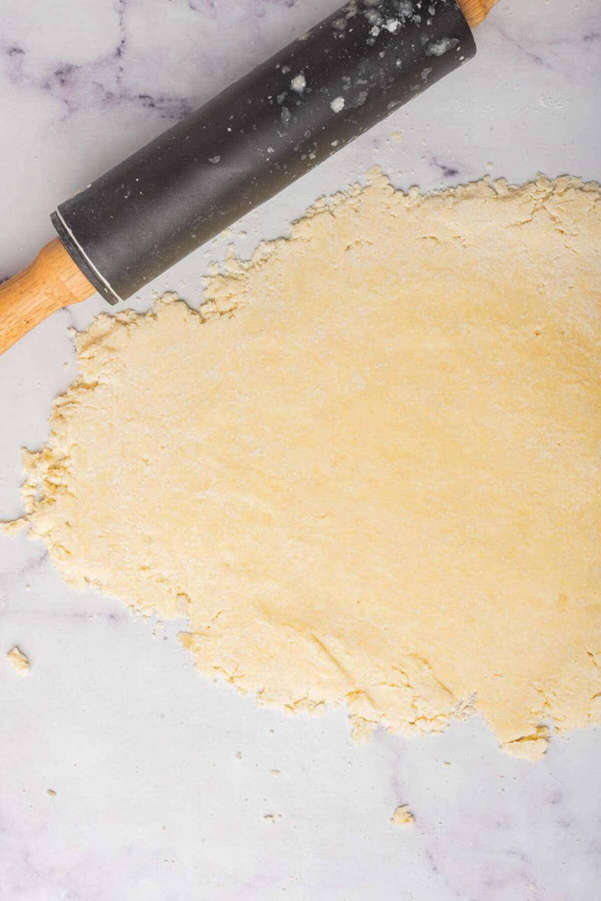 Pie dough on a marble surface, being rolled out with a rolling pin.