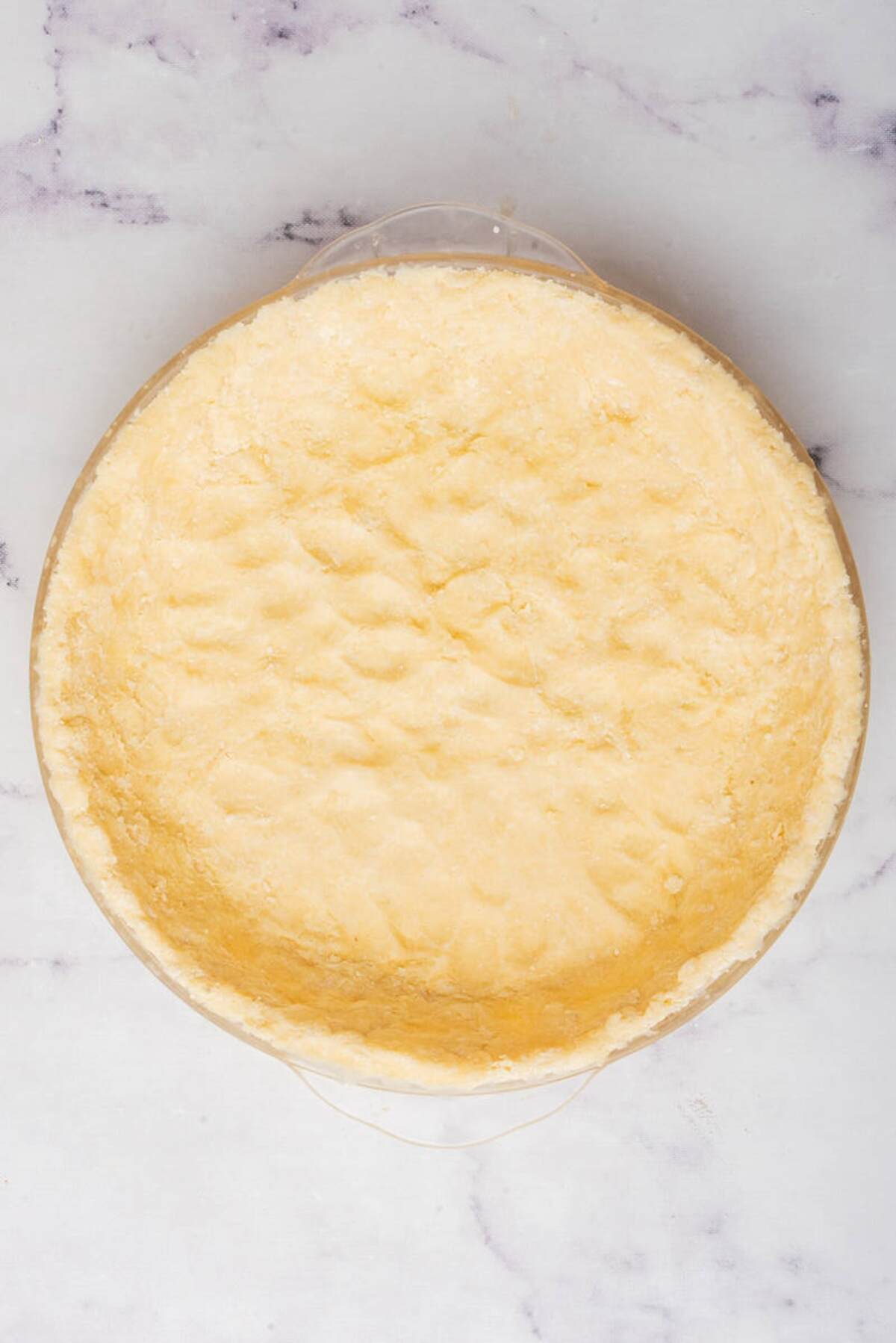 A pie crust in a glass dish, showing the dough neatly pressed and ready for filling.