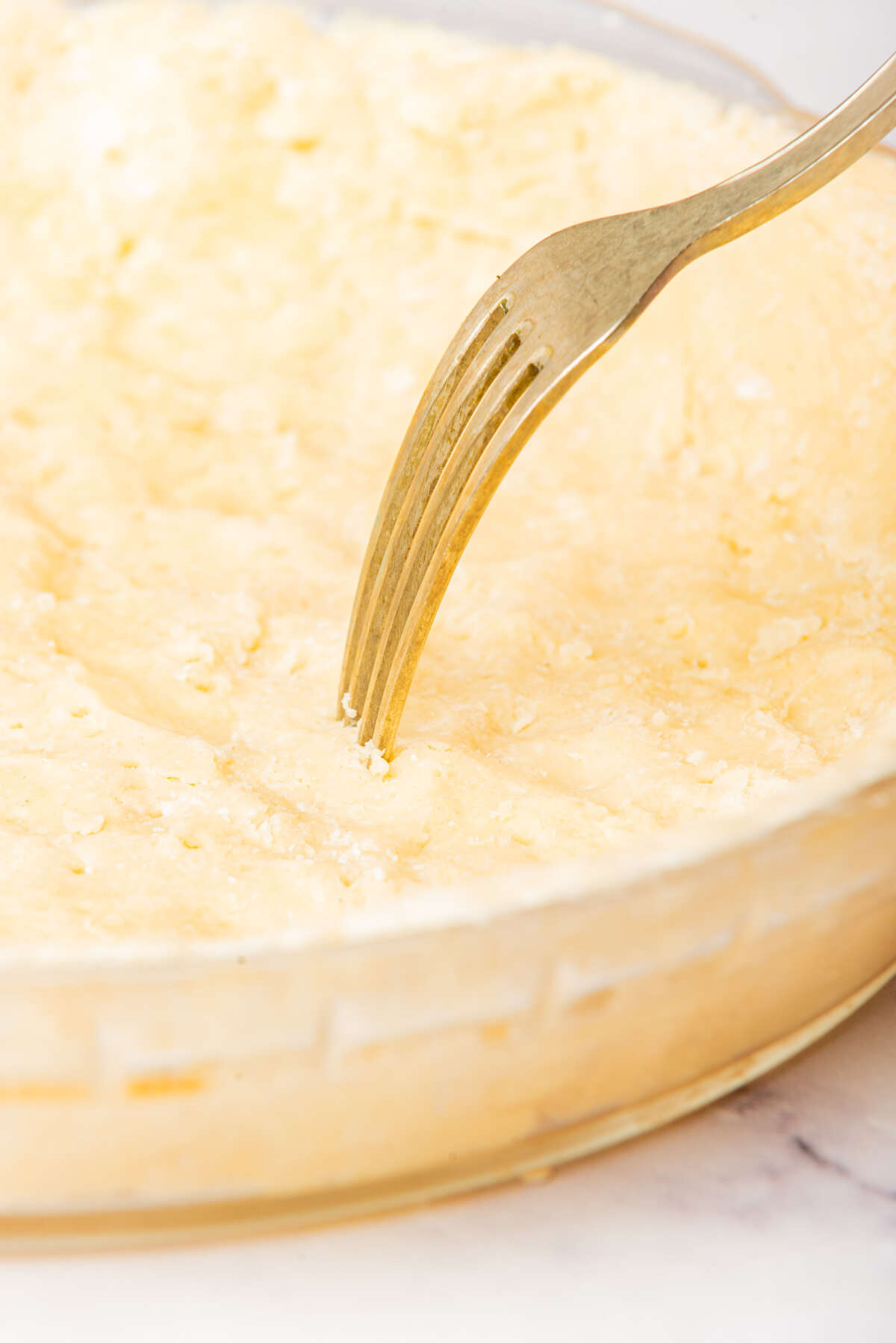 A pie crust being pricked with a fork in a glass pie dish, ensuring even baking.