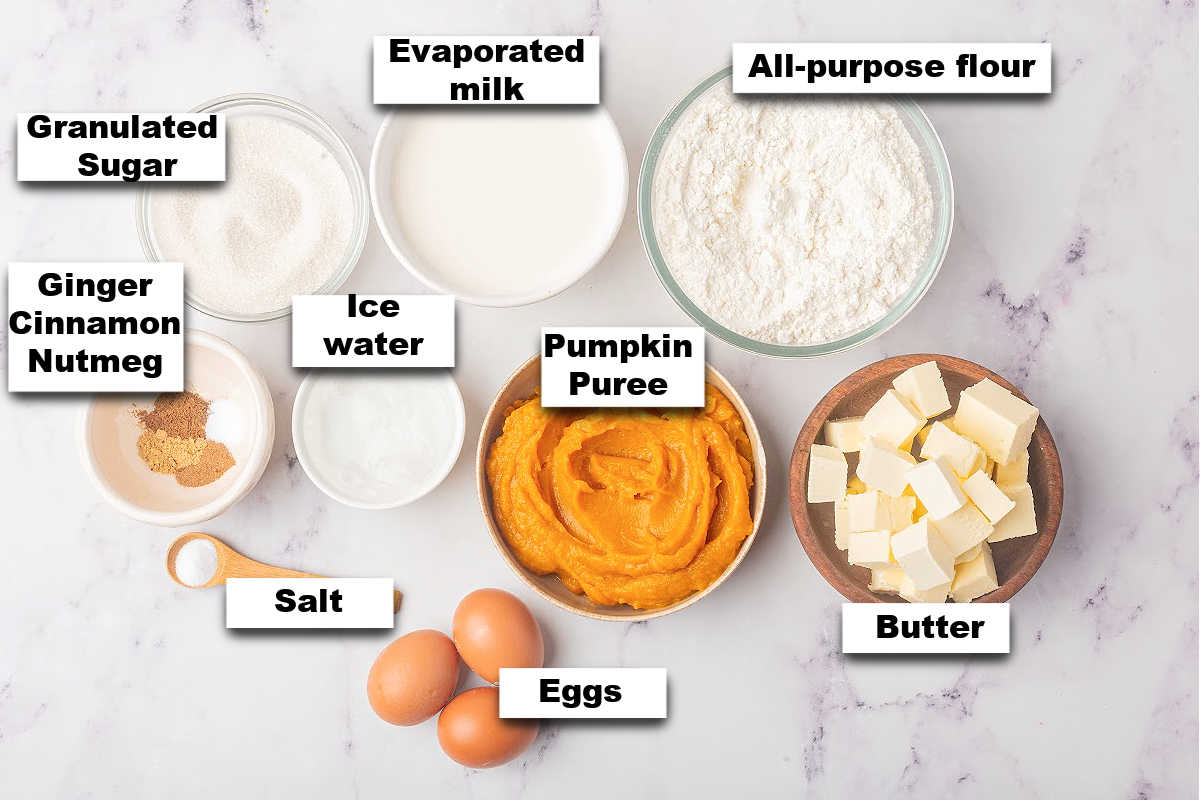Ingredients for making pumpkin pie neatly arranged and labeled on a marble surface.