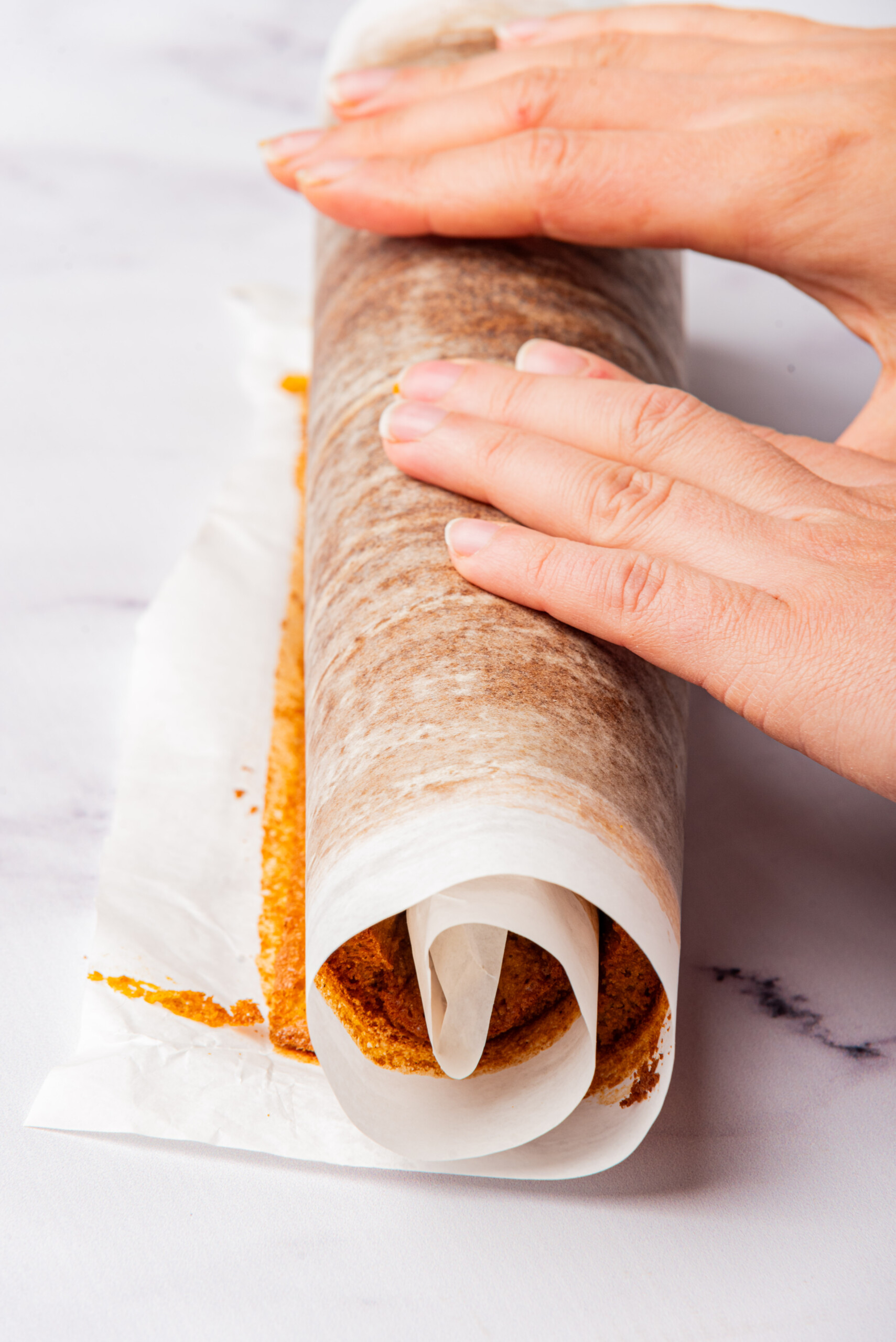 Hands rolling up the baked log cake with parchment paper.