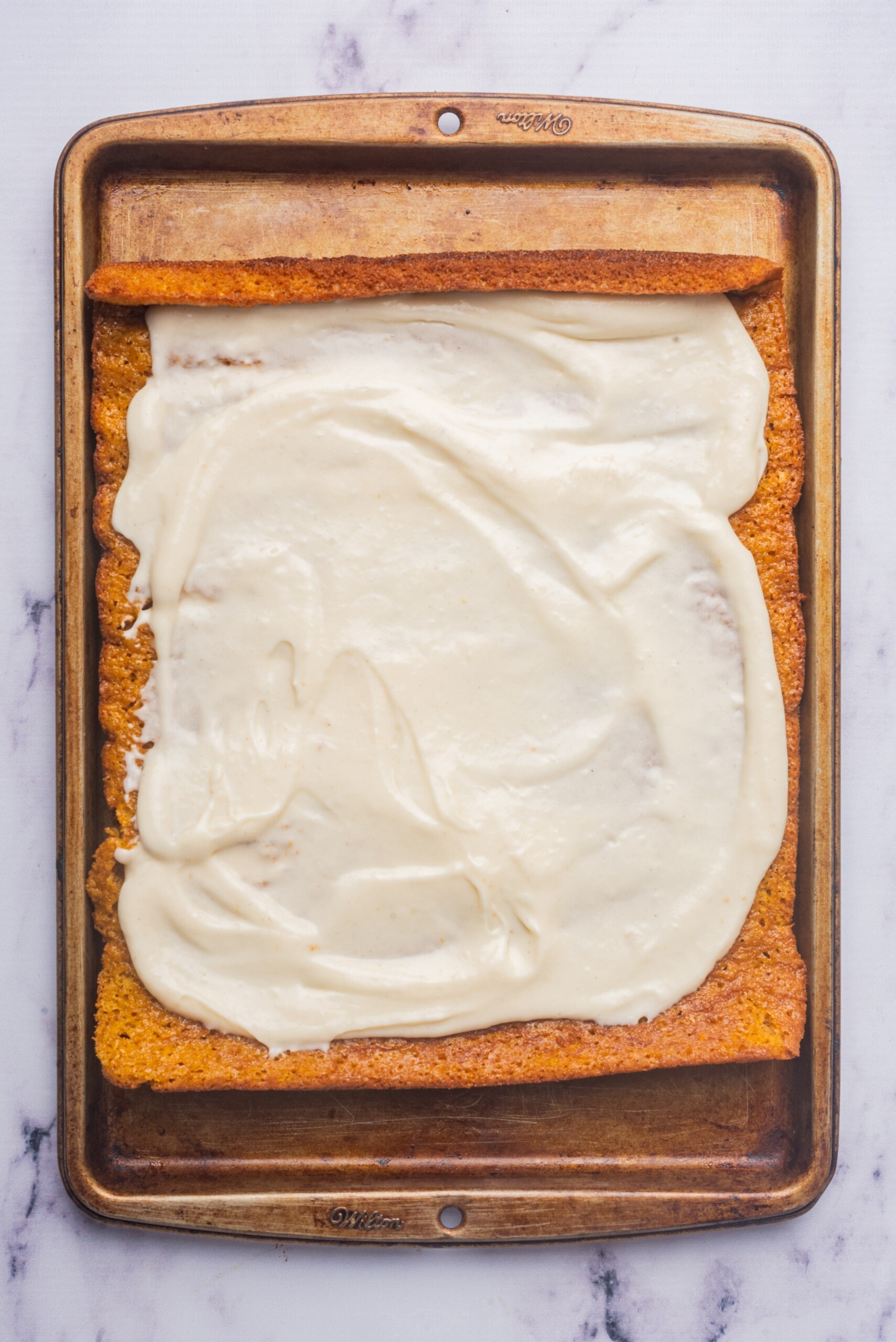 Baked pumpkin roll unrolled and covered with a layer of cream cheese filling on a baking tray.