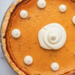 A close-up of a slice of pumpkin pie on a white plate, showcasing the smooth, creamy filling topped with a dollop of whipped cream.