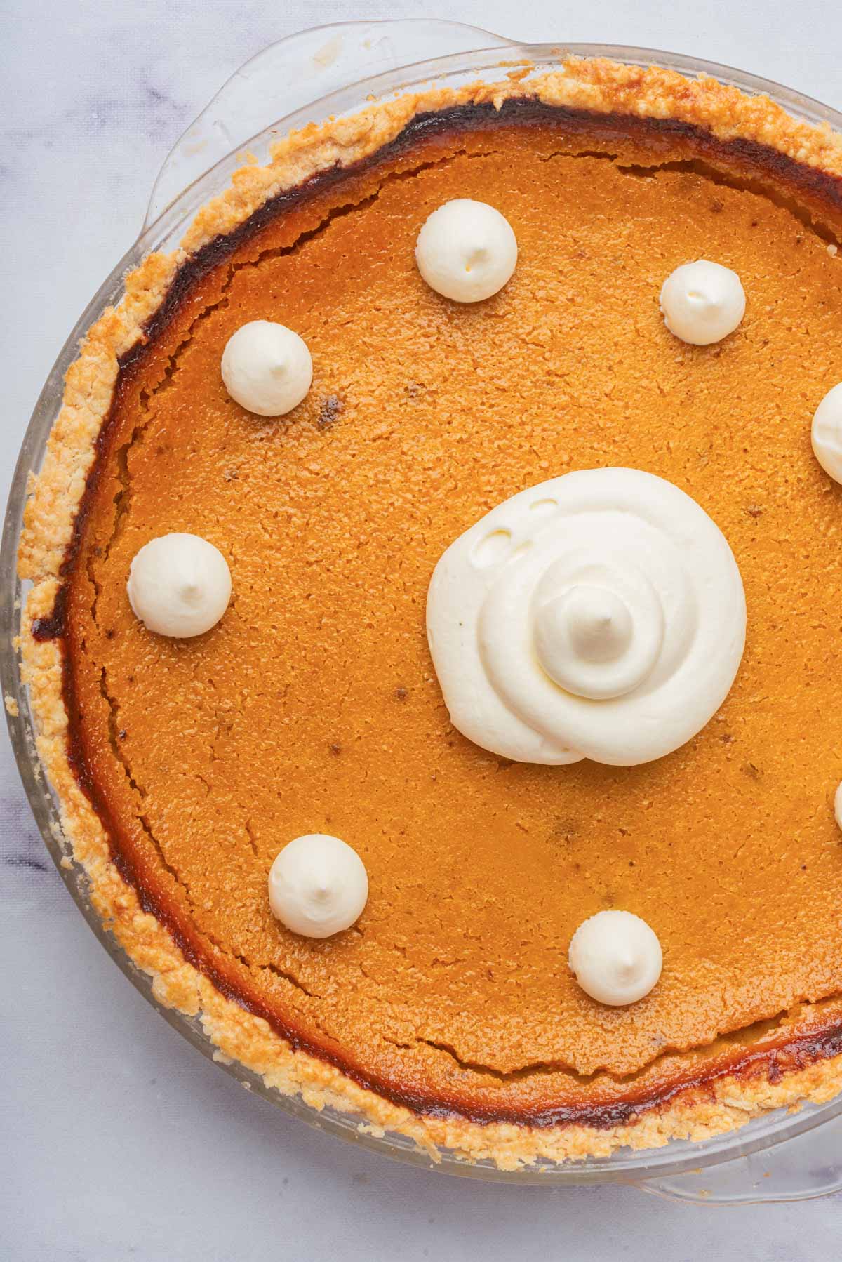 A close-up of a slice of pumpkin pie on a white plate, showcasing the smooth, creamy filling topped with a dollop of whipped cream.