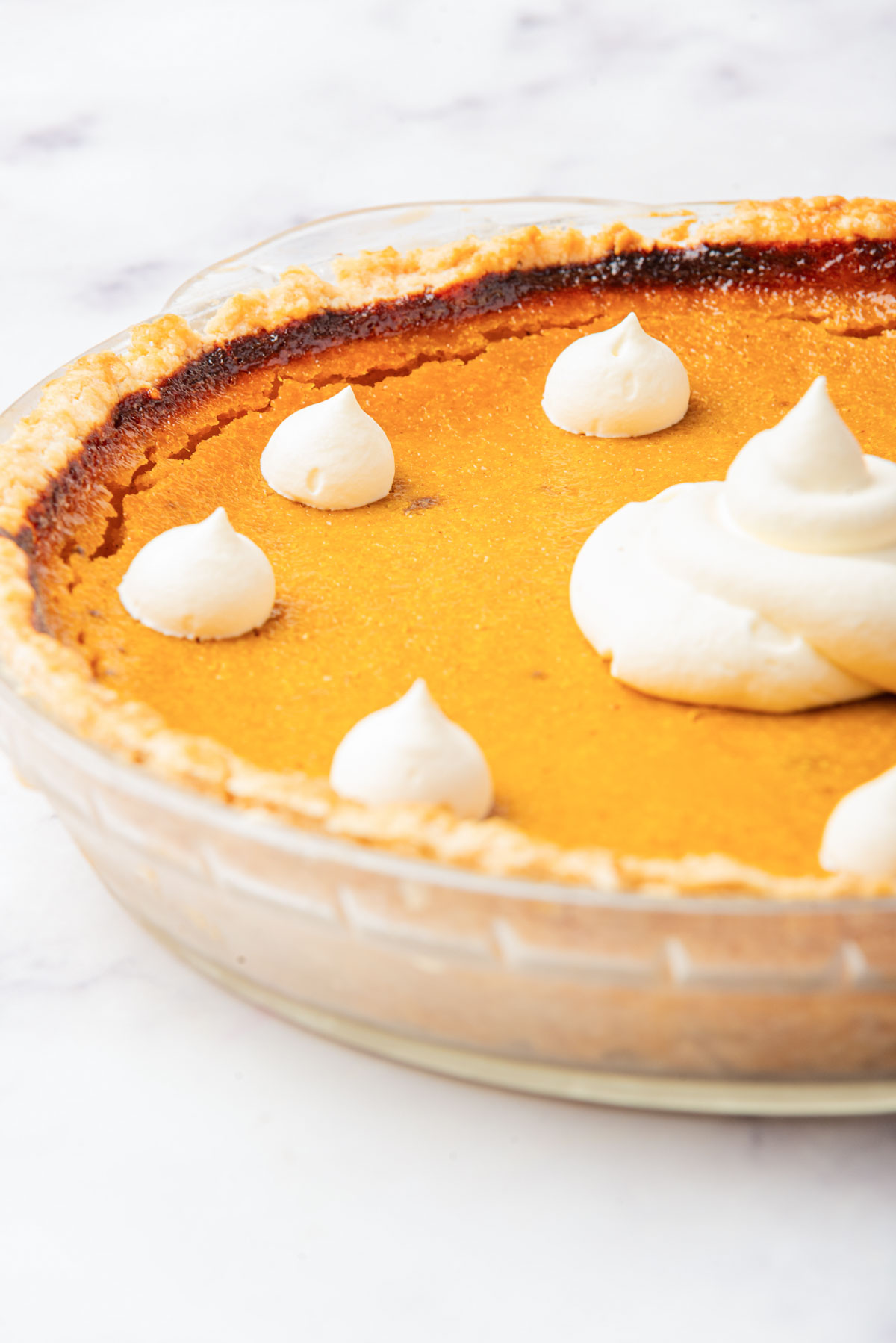 An overhead view of a pumpkin pie with one slice removed, revealing the pie's interior and smooth filling, decorated with dollops of whipped cream.