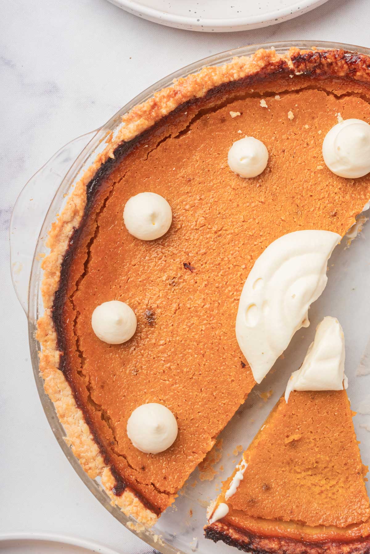 A close-up side view of the whole pumpkin pie with a golden-brown crust, highlighted by several dollops of whipped cream on top and a large swirl in the center.