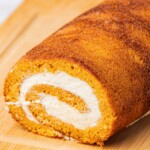 Close-up of a finished pumpkin roll with cream cheese filling on a wooden cutting board.
