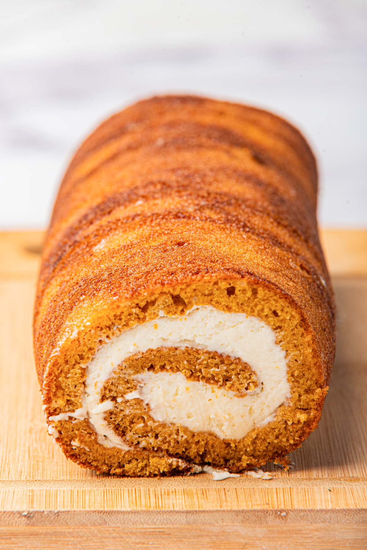 Pumpkin cake with cream cheese filling, showcasing the spiral pattern, placed on a wooden cutting board.