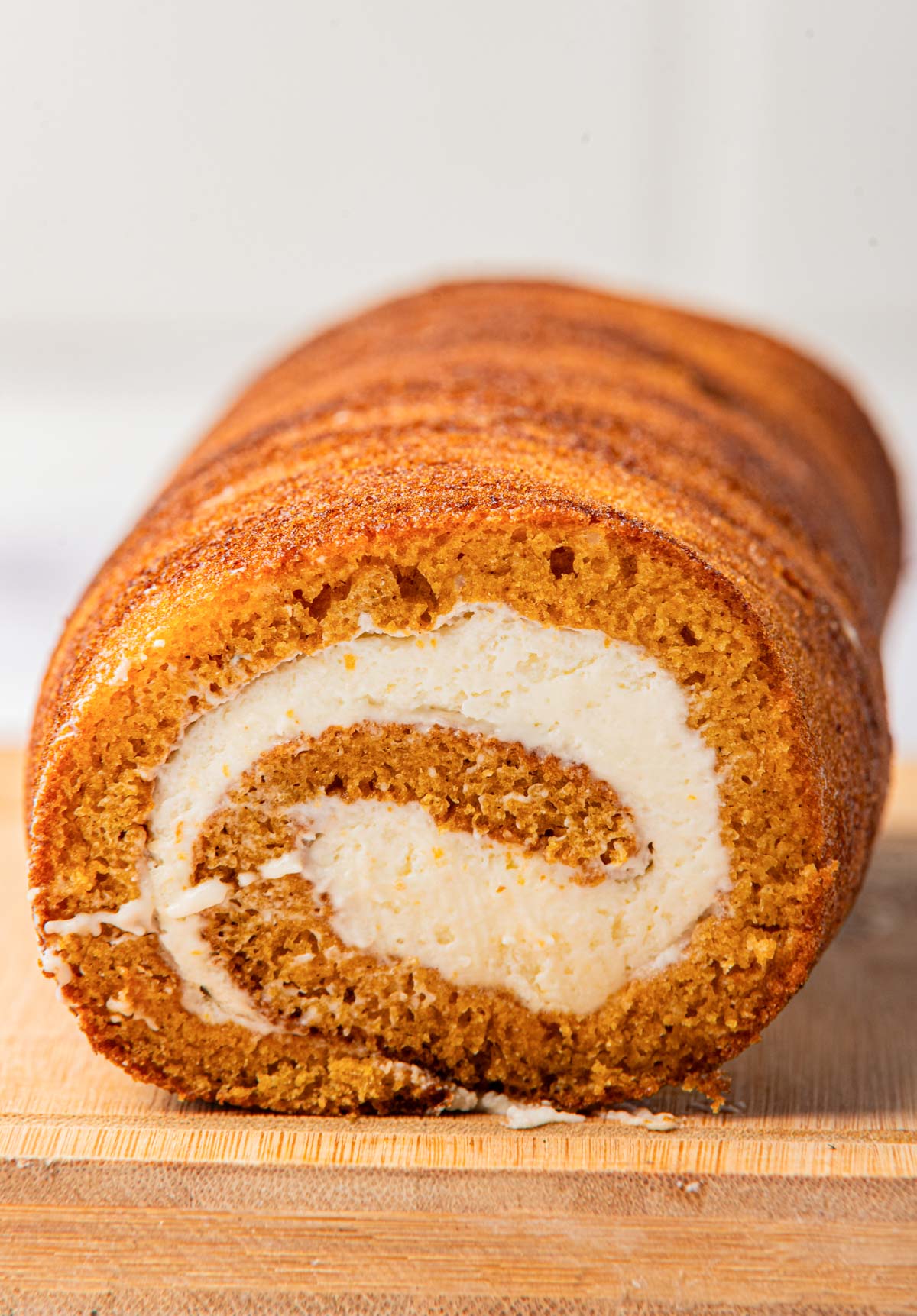 Front view of a pumpkin cake with cream cheese filling, showing the rolled layers on a wooden cutting board.