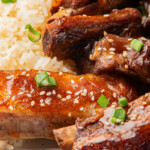 Extreme close-up of saucy pork ribs and fluffy rice, showing crispy edges, sesame seeds, and fresh green onion detail.
