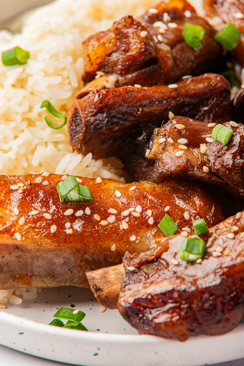 Proche plan de côtes de porc en sauce et riz moelleux, montrant des bords croustillants, des graines de sésame et des oignons verts frais.