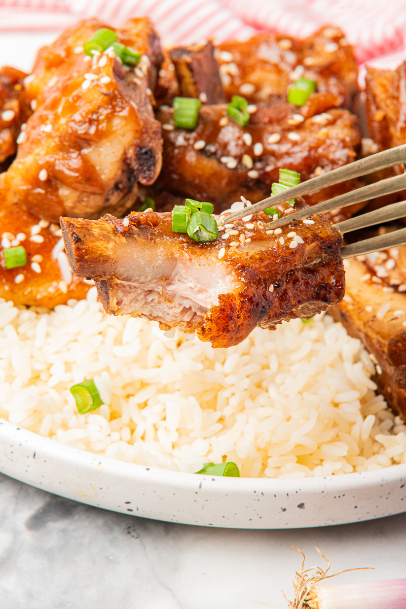Close-up of a single rib held on a fork above a plate of rice, showing the juicy, fall-apart texture inside.