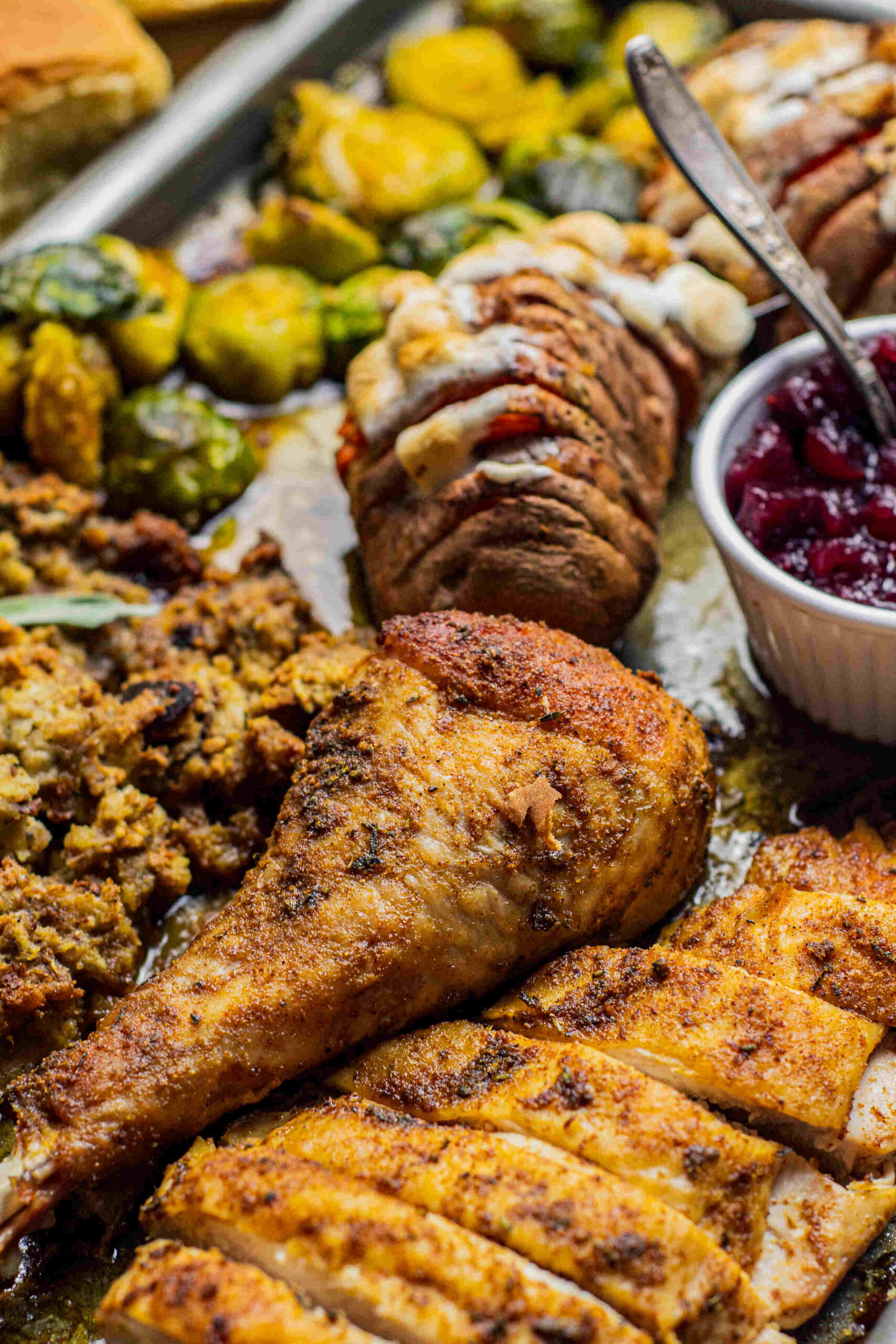 Sheet pan with a turkey dinner with slices of roasted turkey covered in gravy, stuffing, sweet potatoes with marshmallows, Brussels sprouts, asparagus, and a spoonful of cranberry sauce.