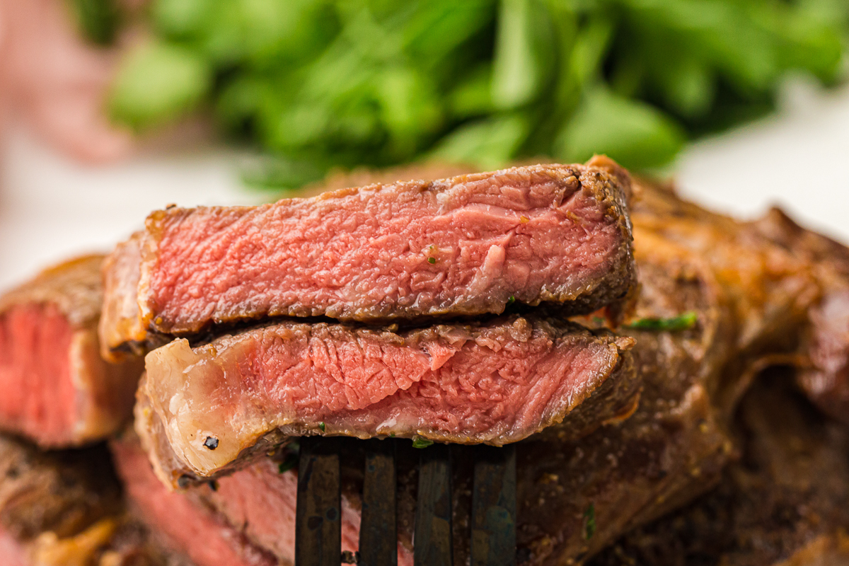 Extreme close-up of a single slice of smoked ribeye steak on a fork, showing the juicy, medium-rare texture and seared edge.