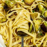 Close-up of pasta with Brussels sprouts and grated cheese in a pan with a fork.