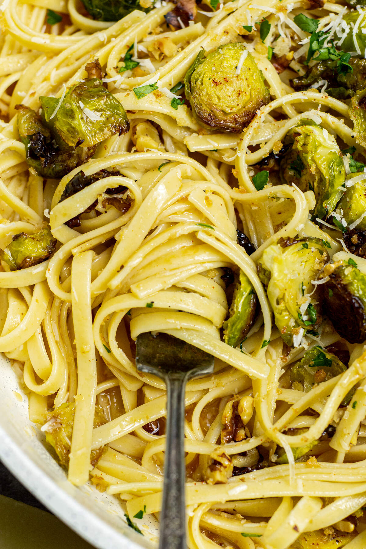 Close-up of pasta with Brussels sprouts and grated cheese in a pan with a fork.