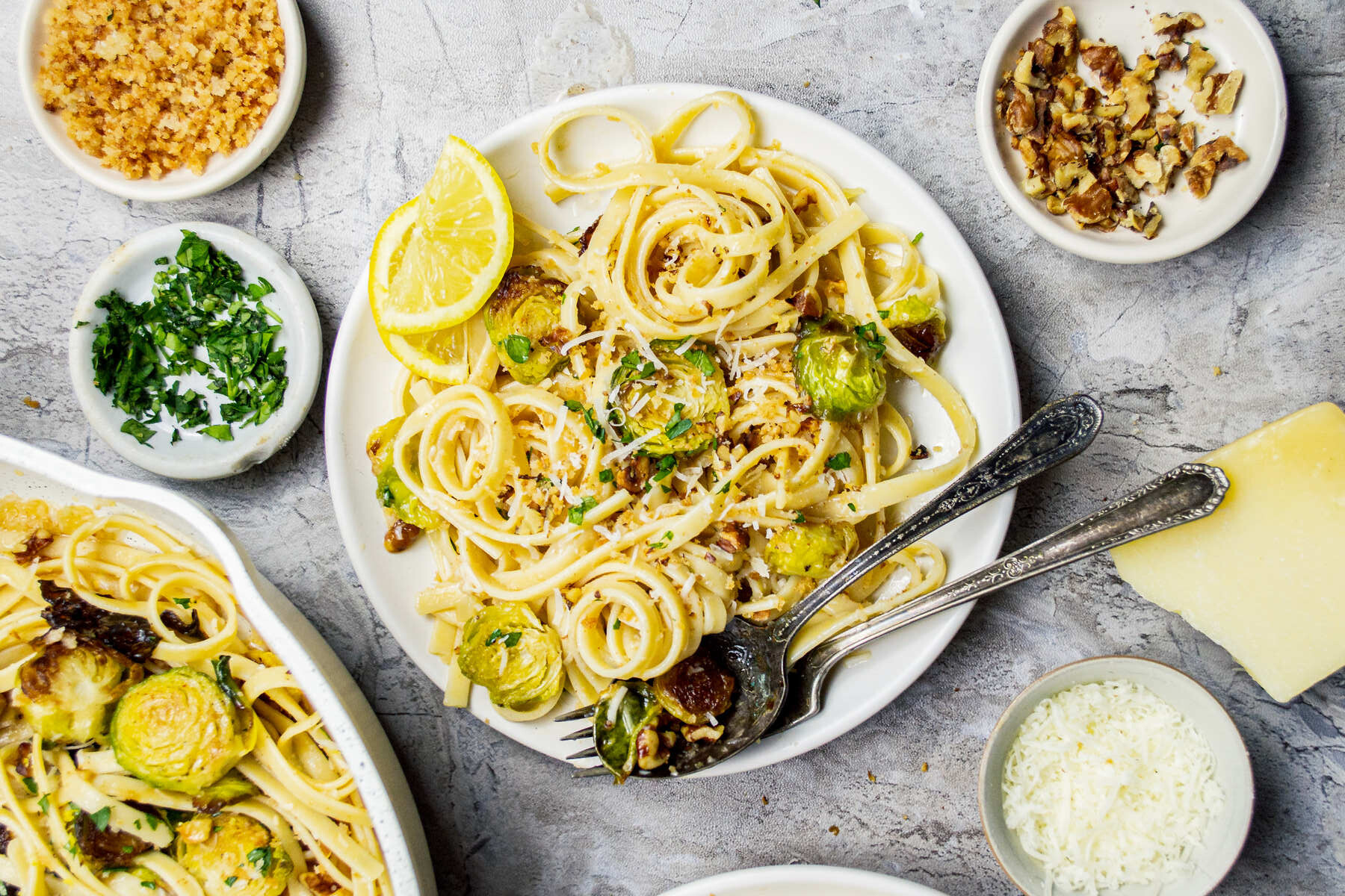 Plate of fettuccine pasta with roasted Brussels sprouts, lemon slices, grated cheese, and chopped parsley.
