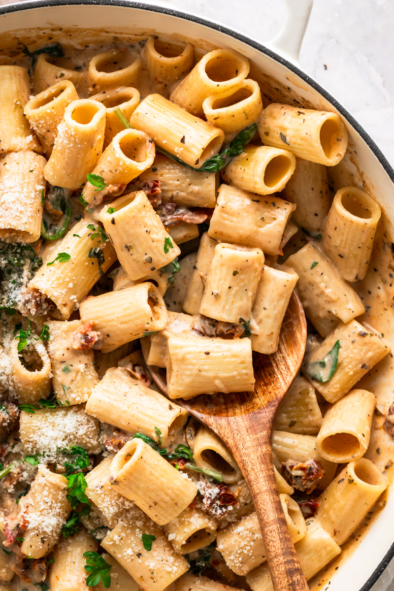 A pot with pasta with sundried tomatoes and a creamy sauce.